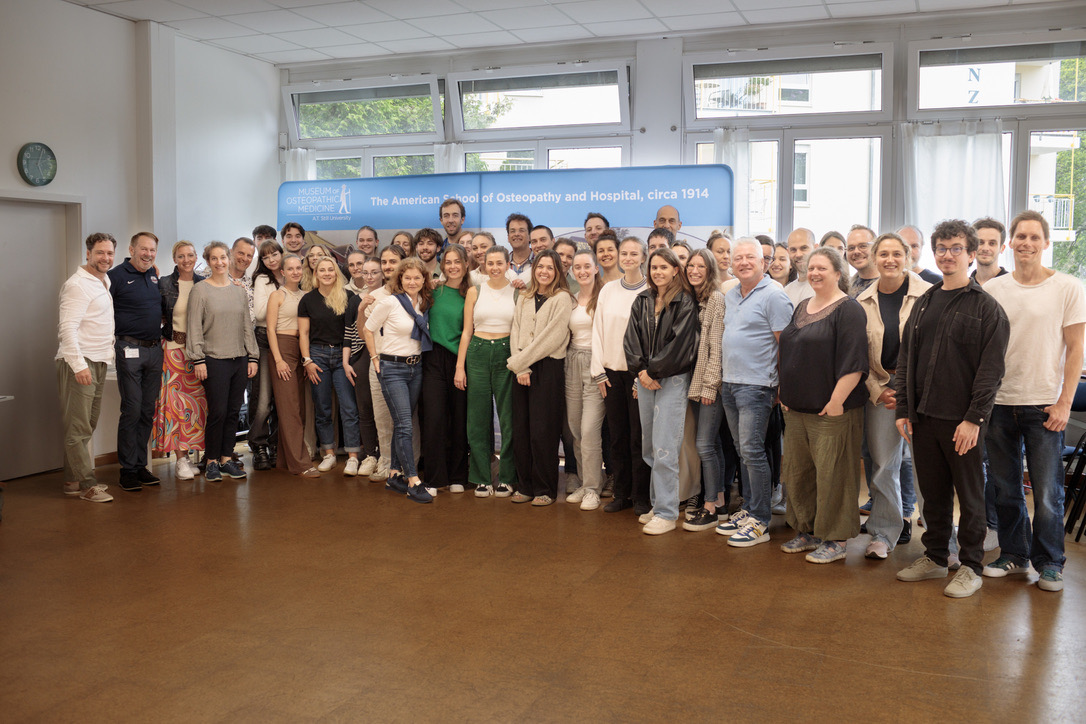 Eine große Gruppe steht gemeinsam in einem hellen Raum und lächelt in die Kamera.